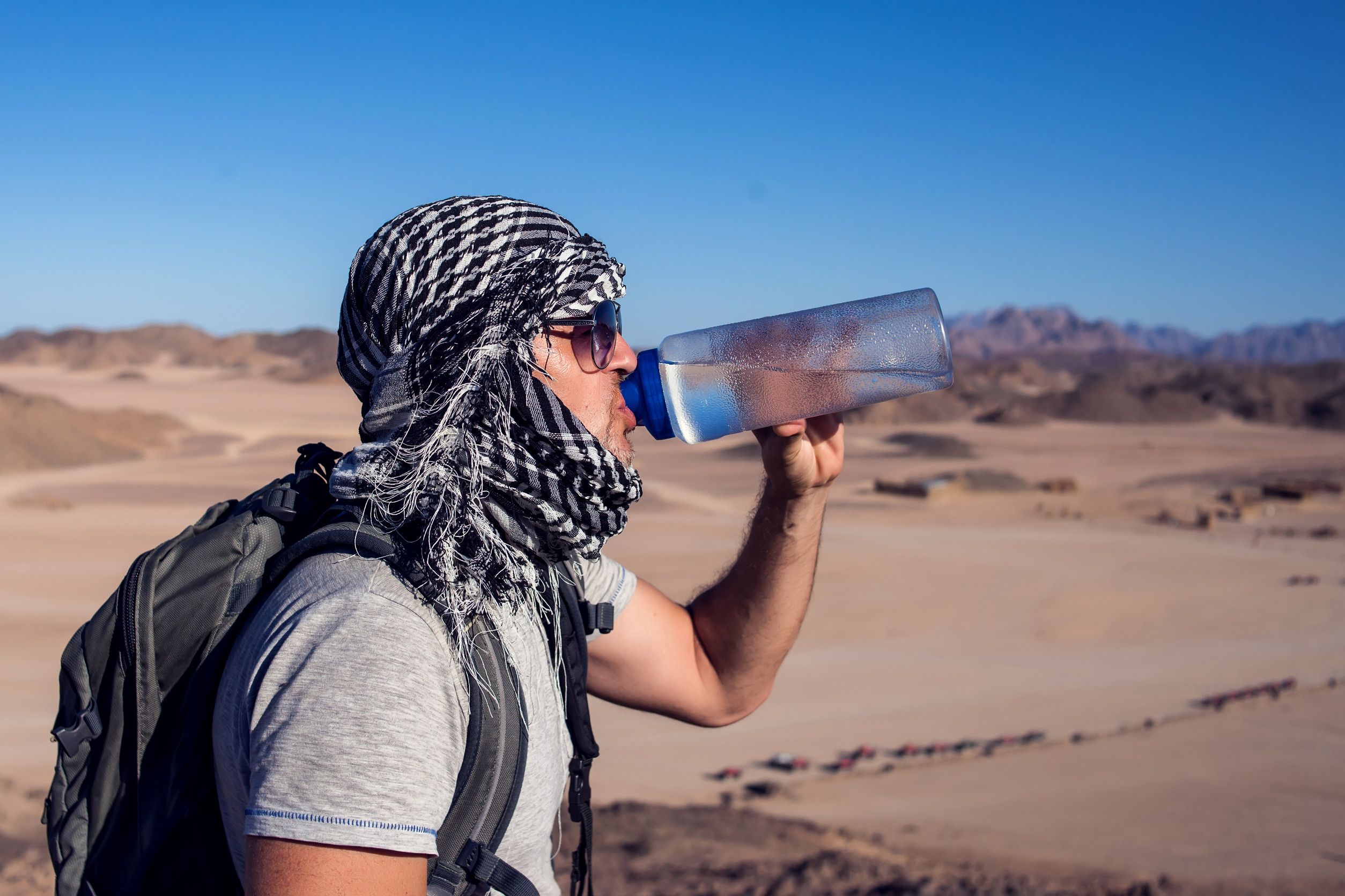 A Man Drinking Water In The Desert To Remain Hydrated