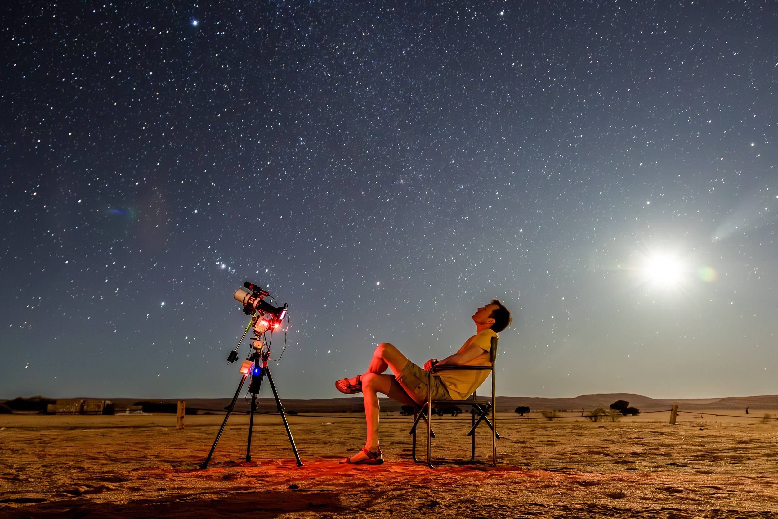 A Man Stargazing In The Arabian Desert Along With A Telescope